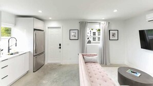 Una habitación moderna y compacta con kitchenette, cama, televisor y ventana con cortinas.