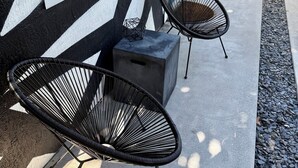 Dos sillas de estructura de alambre negro sobre una plataforma de concreto frente a un edificio con fachada blanco y negro.