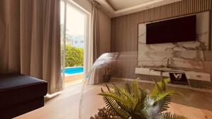 Ein modernes Wohnzimmer mit großem Fernseher, einer Couch, einem Esstisch und Blick auf einen Swimmingpool.