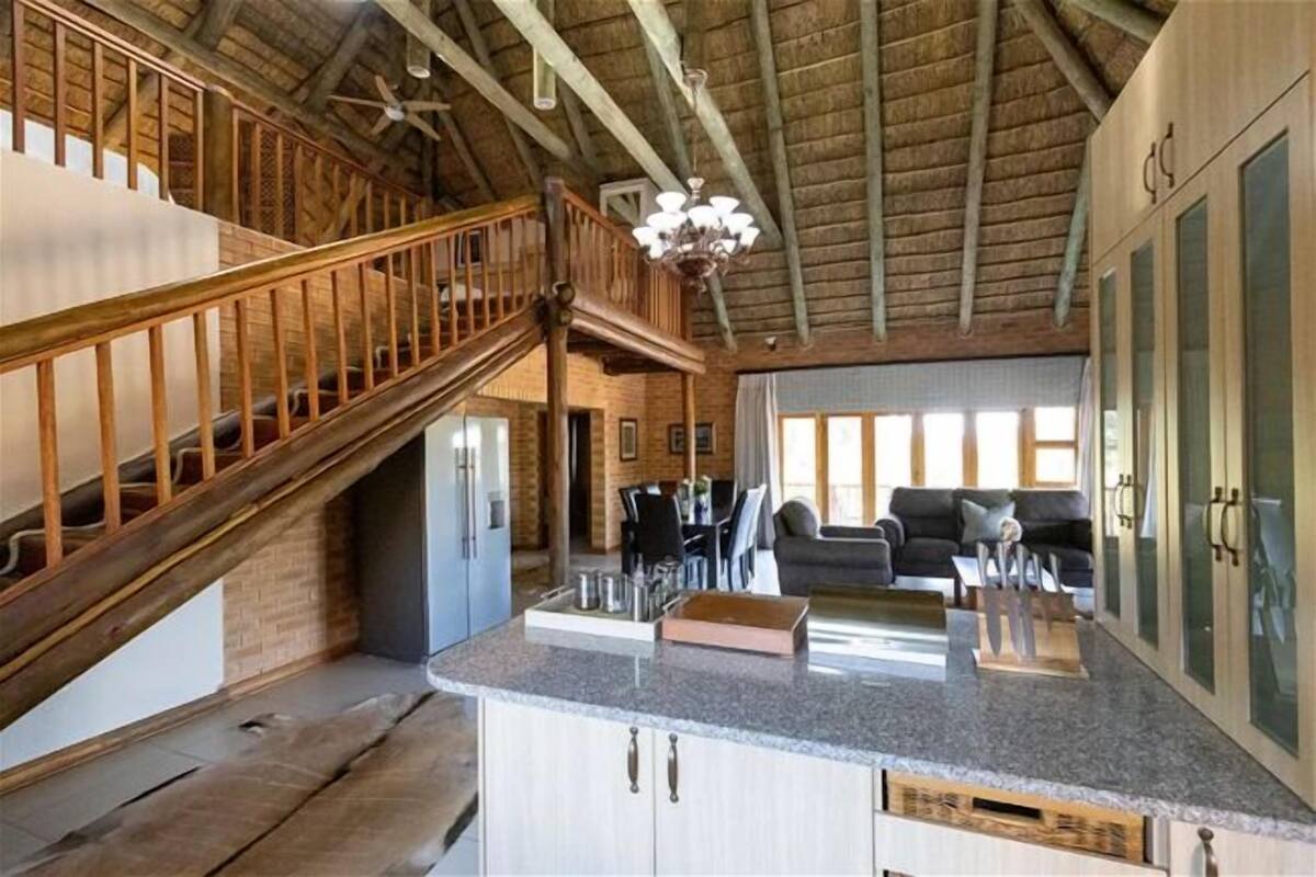 A spacious kitchen with a granite countertop, wooden staircase, and a dining area with a sofa and table.