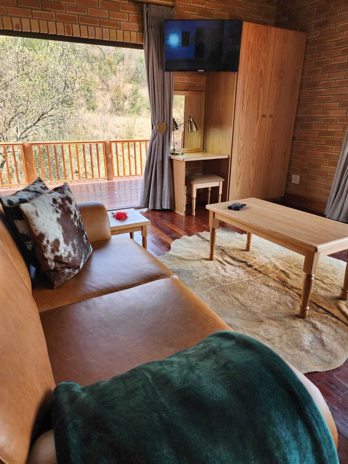 Una habitación acogedora con un sofá de madera, una mesita, un televisor montado en la pared y vistas al exterior.