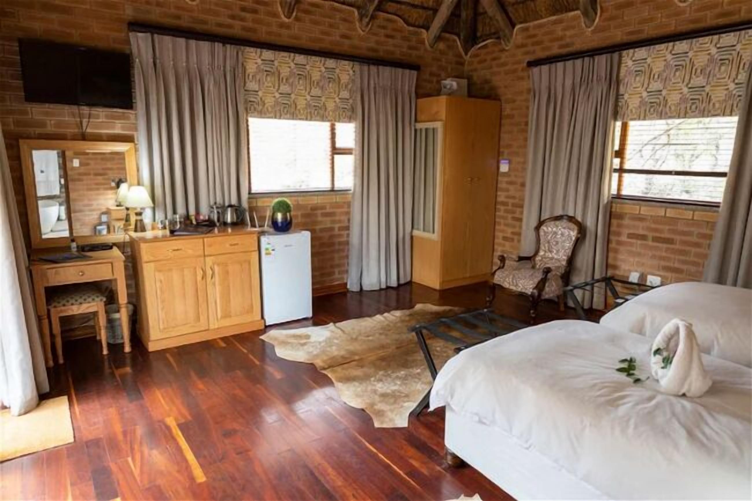A room with a wooden desk, a bed, a chair, and a small refrigerator.