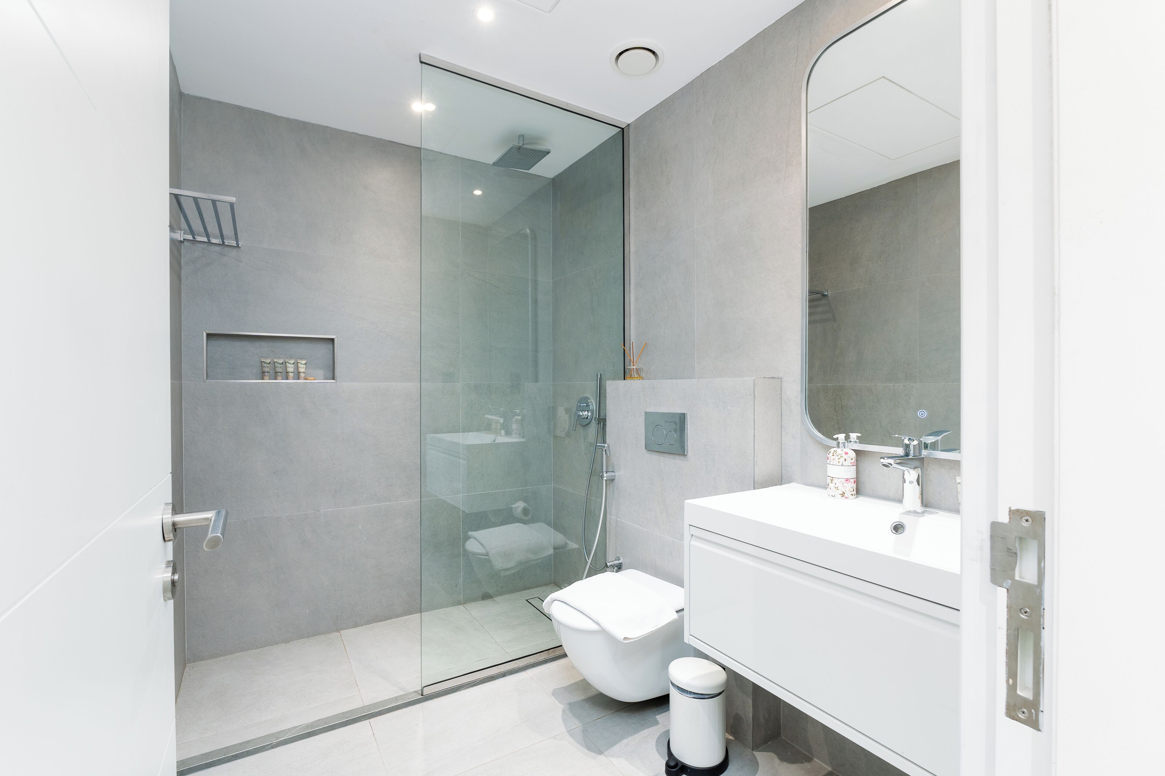A modern bathroom with a glass-enclosed shower, a white toilet, and a vanity with a mirror.