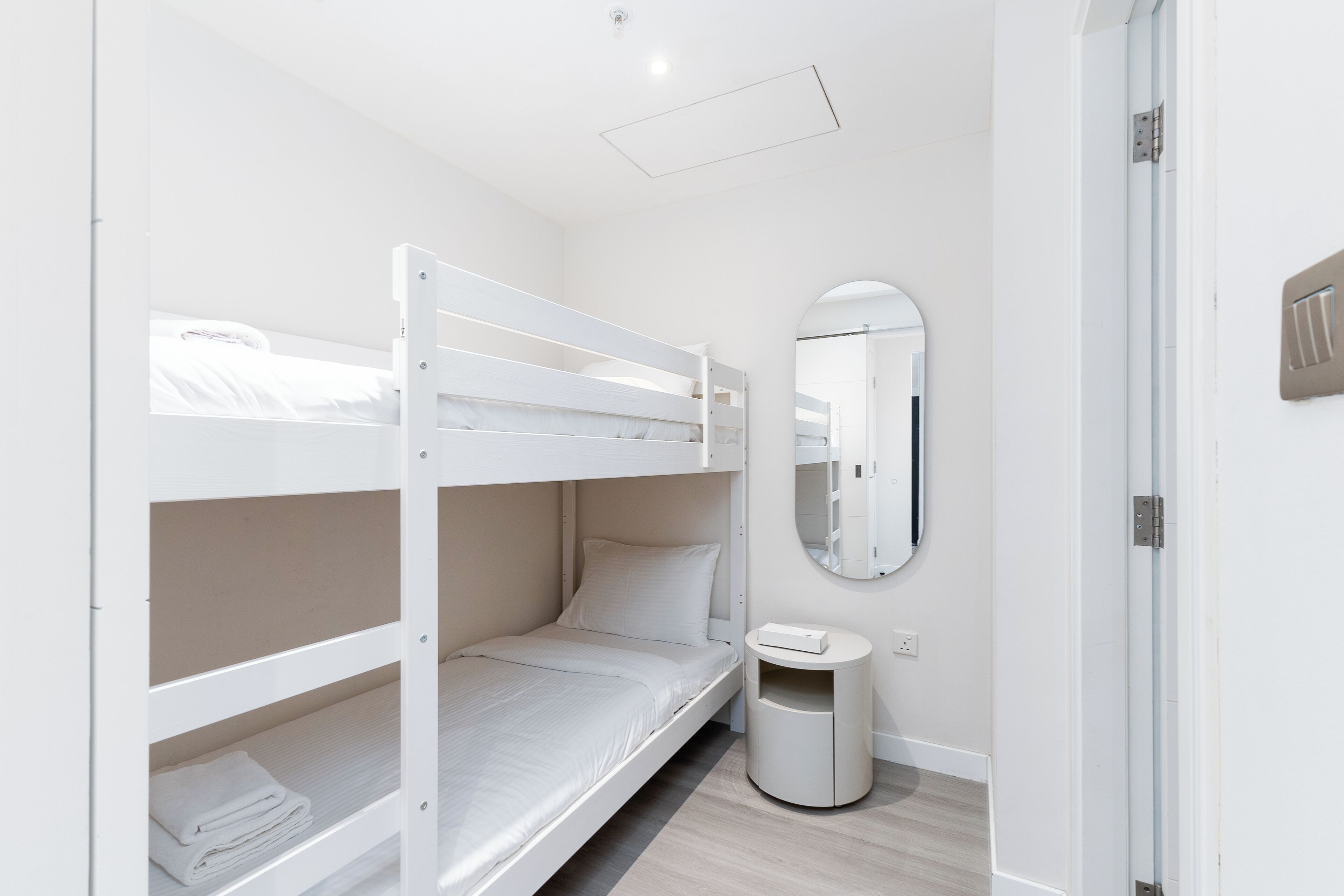 A bunk bed room with a small bedside table and a mirror.