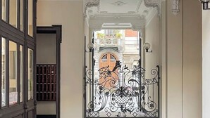 Een sierlijk ijzeren hekwerk met ingewikkelde ontwerpen, dat leidt naar een balkon met uitzicht op een gebouw met een rode deur.