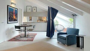 Een moderne woonkamer met een eethoek, een blauwe bank en een groot raam met gordijnen.