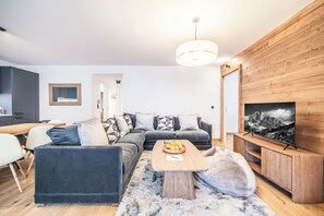 Ein modernes Wohnzimmer mit einem dunkelgrauen Sofa, einem Holztisch und einem Fernseher auf einem Holzschrank.
