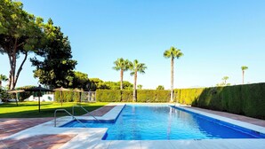 A rectangular swimming pool with a tiled deck, surrounded by palm trees and a well-maintained hedge. - Genteel Home Casa Aloha Golf (Marbella)