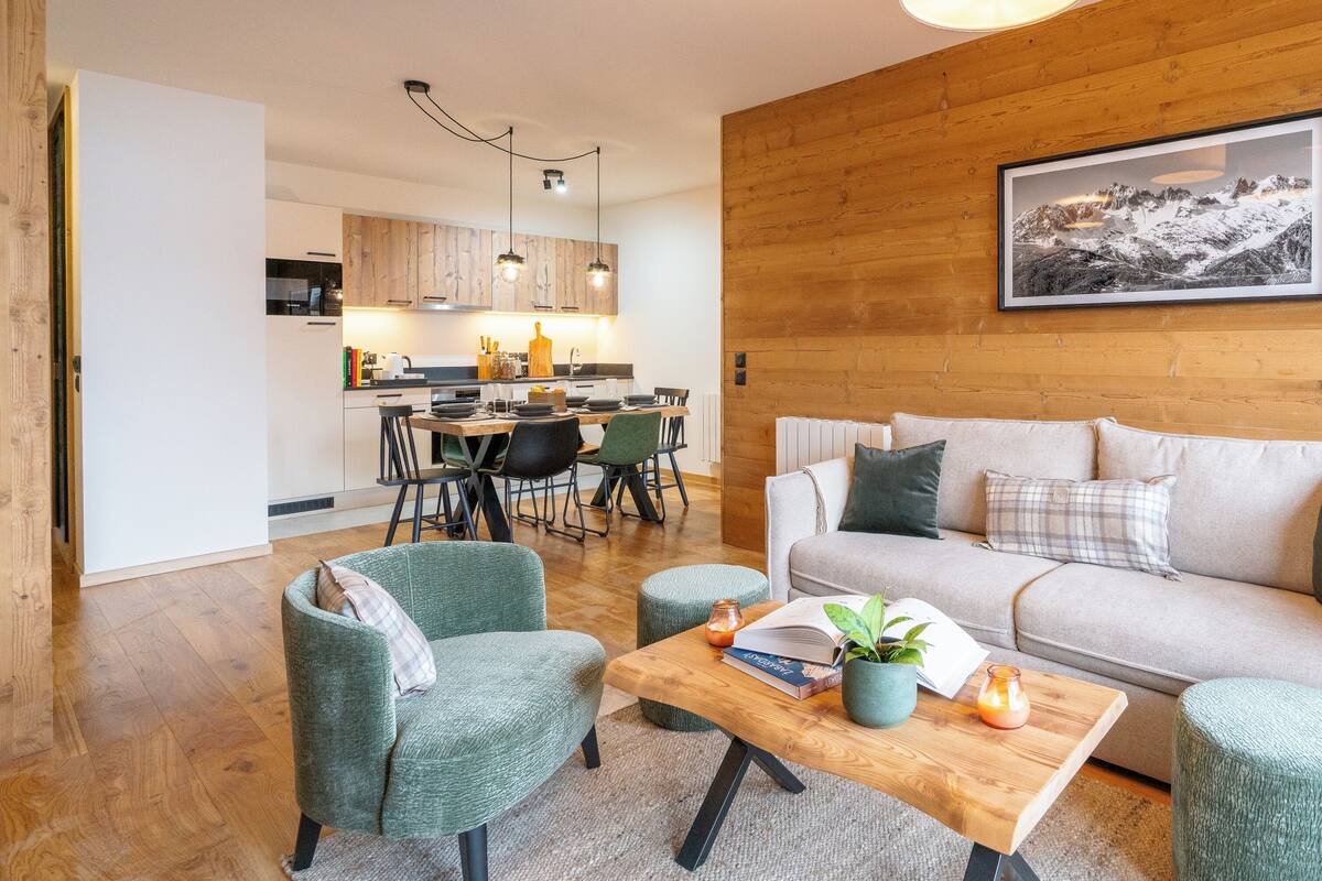 A modern living room with a wooden wall, a sofa, two armchairs, a coffee table, and a dining area in the background.