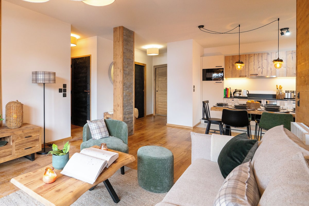 A modern living room with a wooden coffee table, a sofa, and a dining area with a kitchen in the background.