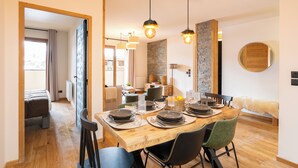 A dining area with a wooden table set for four, surrounded by chairs. There are hanging pendant lights above the table. - Résidence l'Alpeggio by My Mountain Resort (Les Deux Alpes)