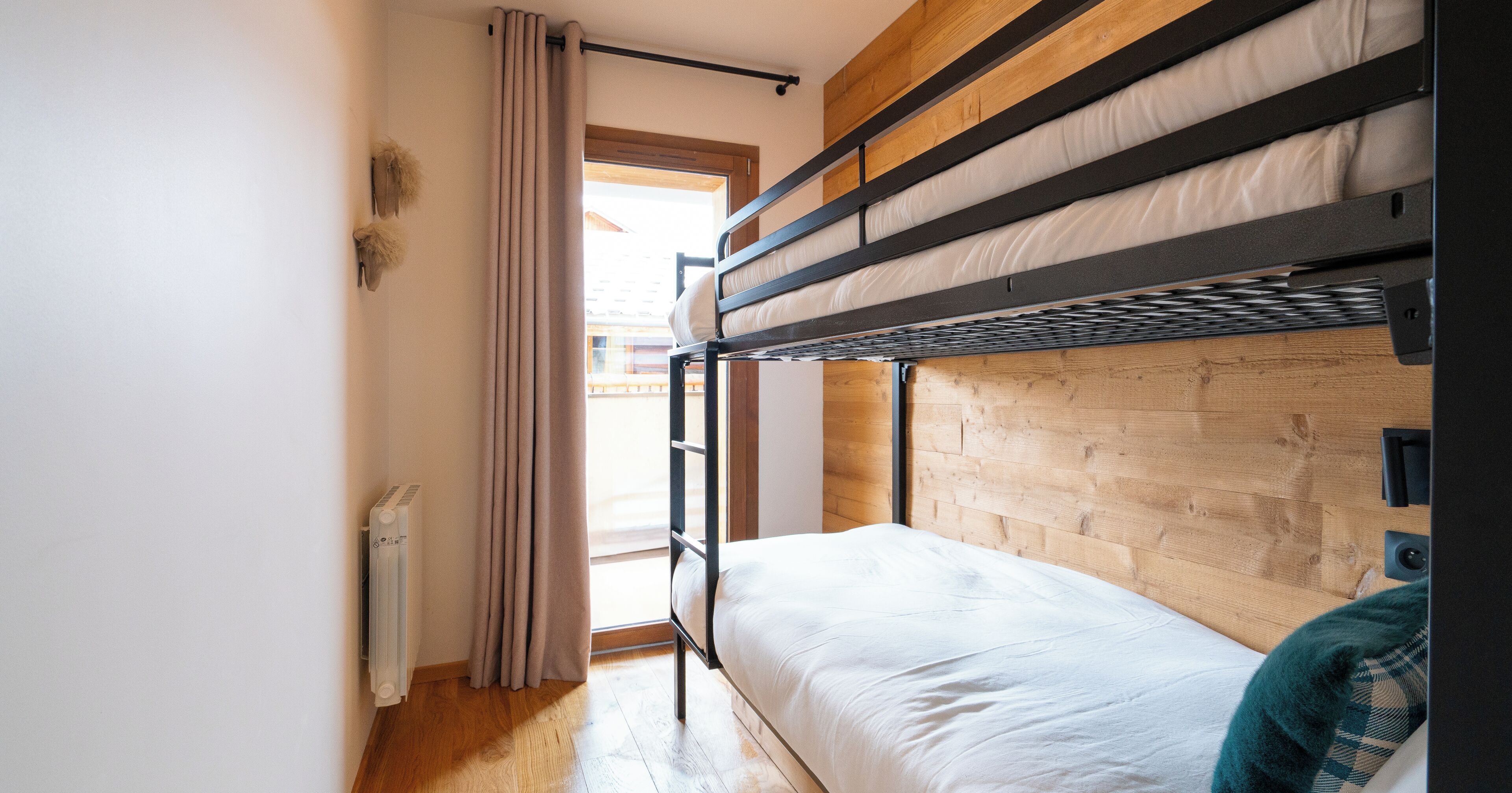 A bunk bed room with a wooden headboard, a radiator, and a window with curtains.