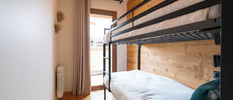A bunk bed room with a wooden headboard, a radiator, and a window with curtains.