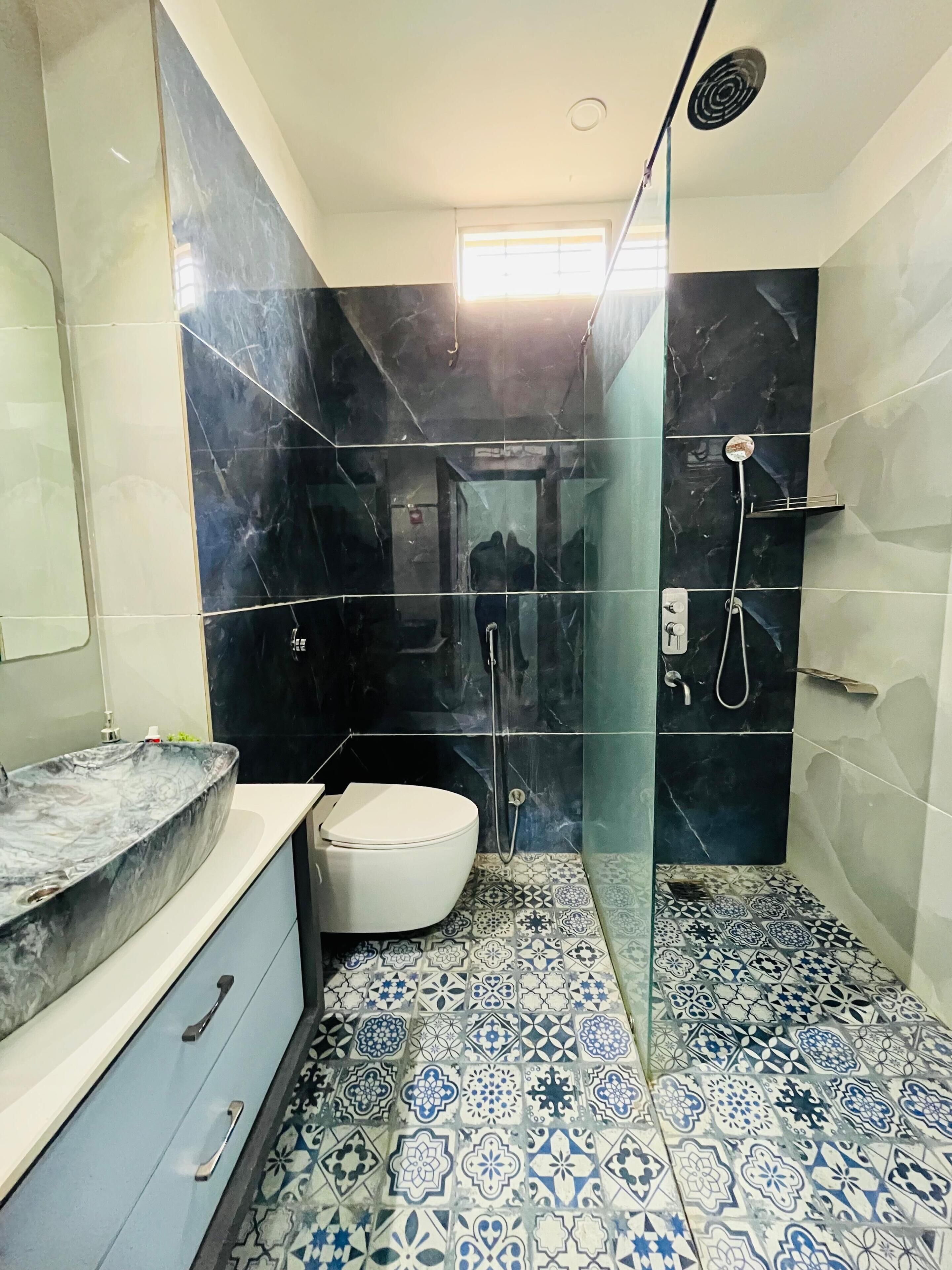 A bathroom with a marble sink, a toilet, a shower with a glass door, and patterned floor tiles.