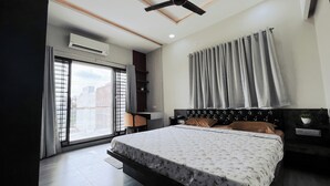 A modern bedroom with a large bed, a desk, and a window with curtains. - Shyamsudha Homestay (Ujjain)