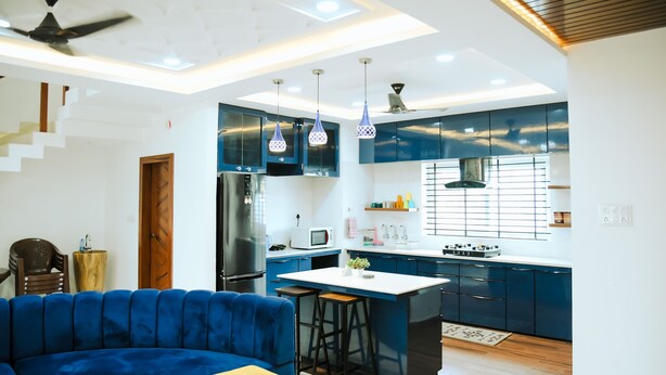 A modern kitchen with blue cabinets, a stainless steel refrigerator, and a gas stove. - Shyamsudha Homestay (Ujjain)