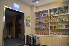 A hotel lobby with a reception desk, a potted plant, and shelves stocked with snacks and toiletries. - Shankee Hotel (Zibo Badaju RT-Mart) (Zibo)