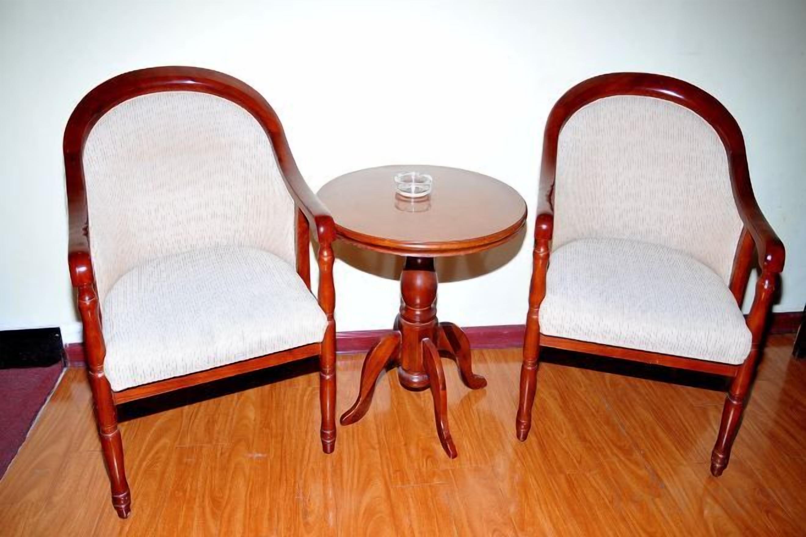 Duas cadeiras de madeira com assentos e encostos acolchoados, uma pequena mesa redonda de madeira com um copo e um chão de madeira.