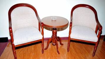 Duas cadeiras de madeira com assentos e encostos acolchoados, uma pequena mesa redonda de madeira com um copo e um chão de madeira.