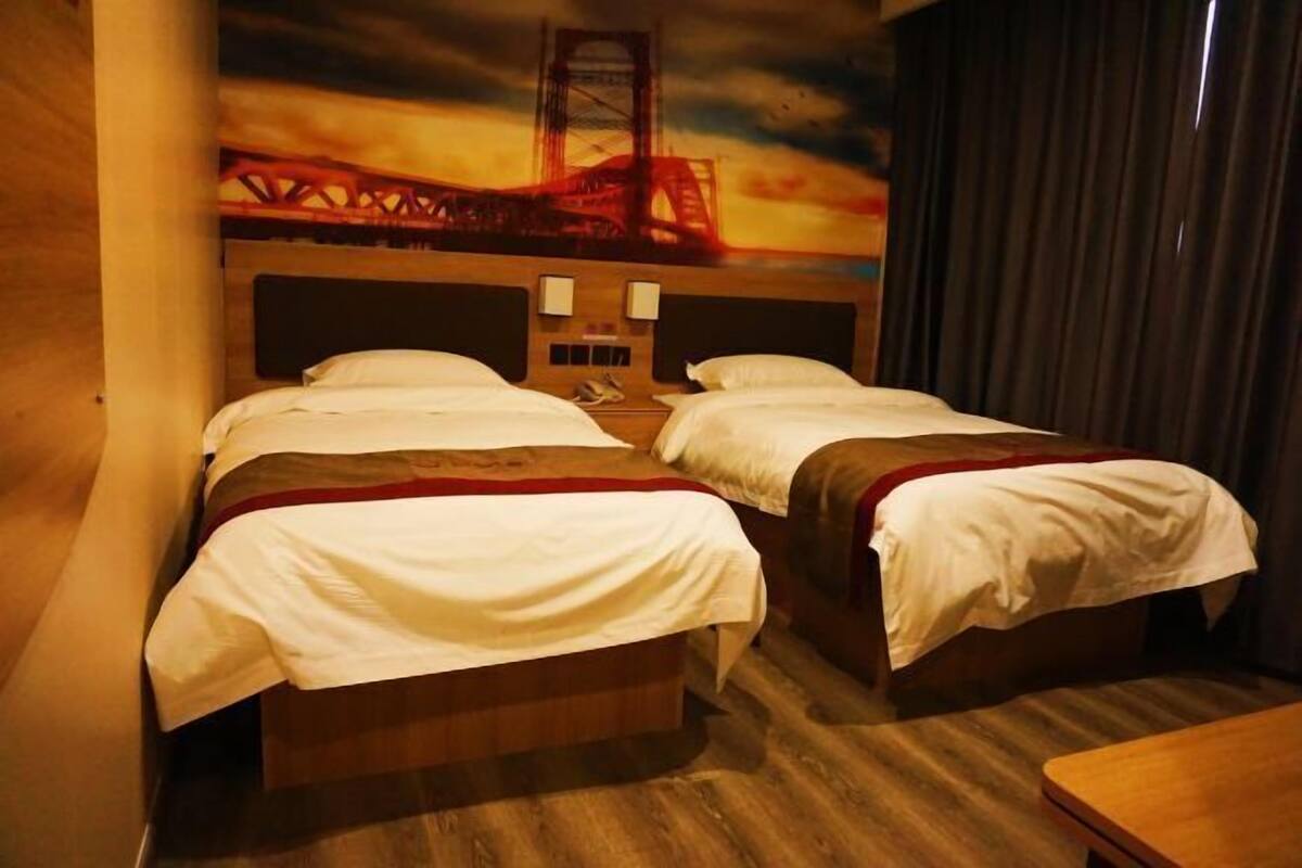 Une chambre d’hôtel avec deux lits, une tête de lit en bois, une table de chevet et une fresque représentant un pont.