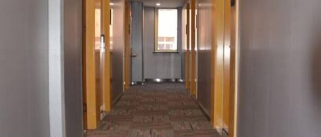 Un pasillo con piso alfombrado, puertas de madera y una ventana al final.