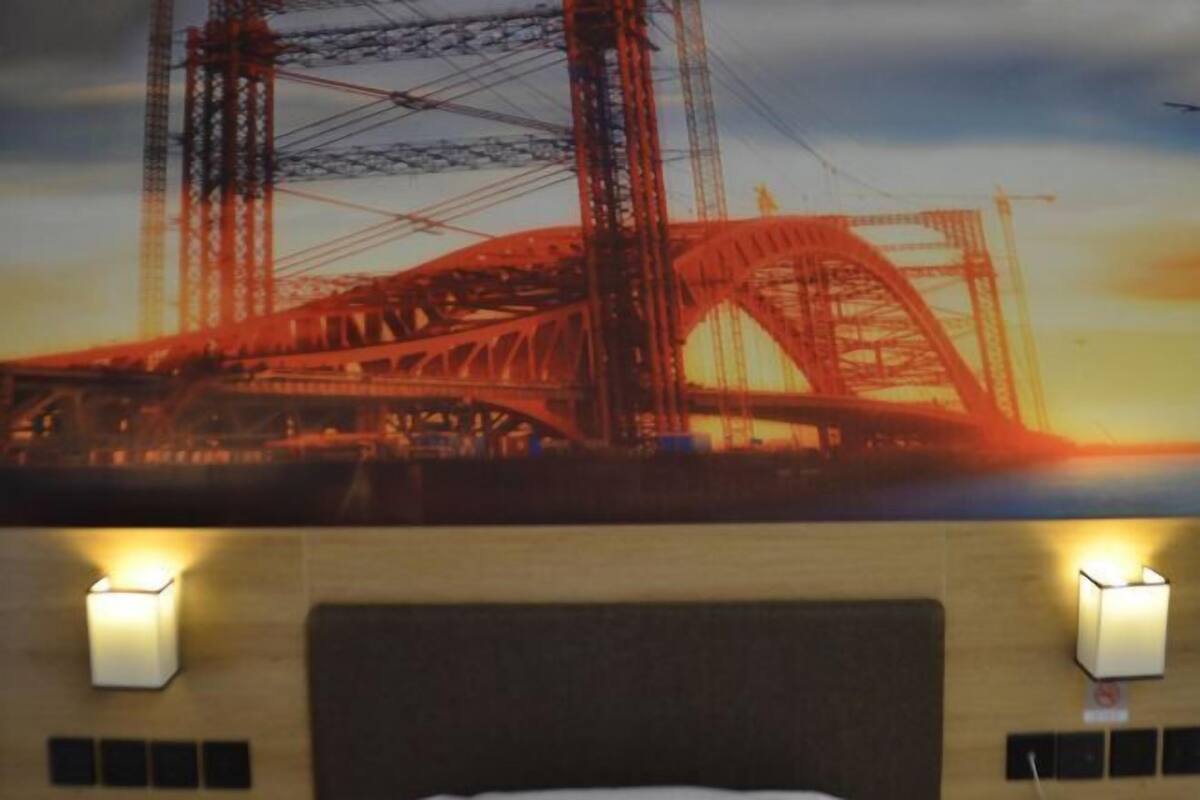 Une chambre d’hôtel avec un grand lit, deux appliques murales et une vue sur un pont en construction.