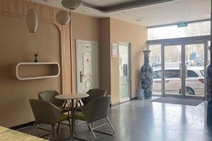 A hotel lobby with a reception desk, a seating area with chairs, a vase, and a door leading outside. - Shankee Hotel (Zibo Badaju RT-Mart) (Zibo)