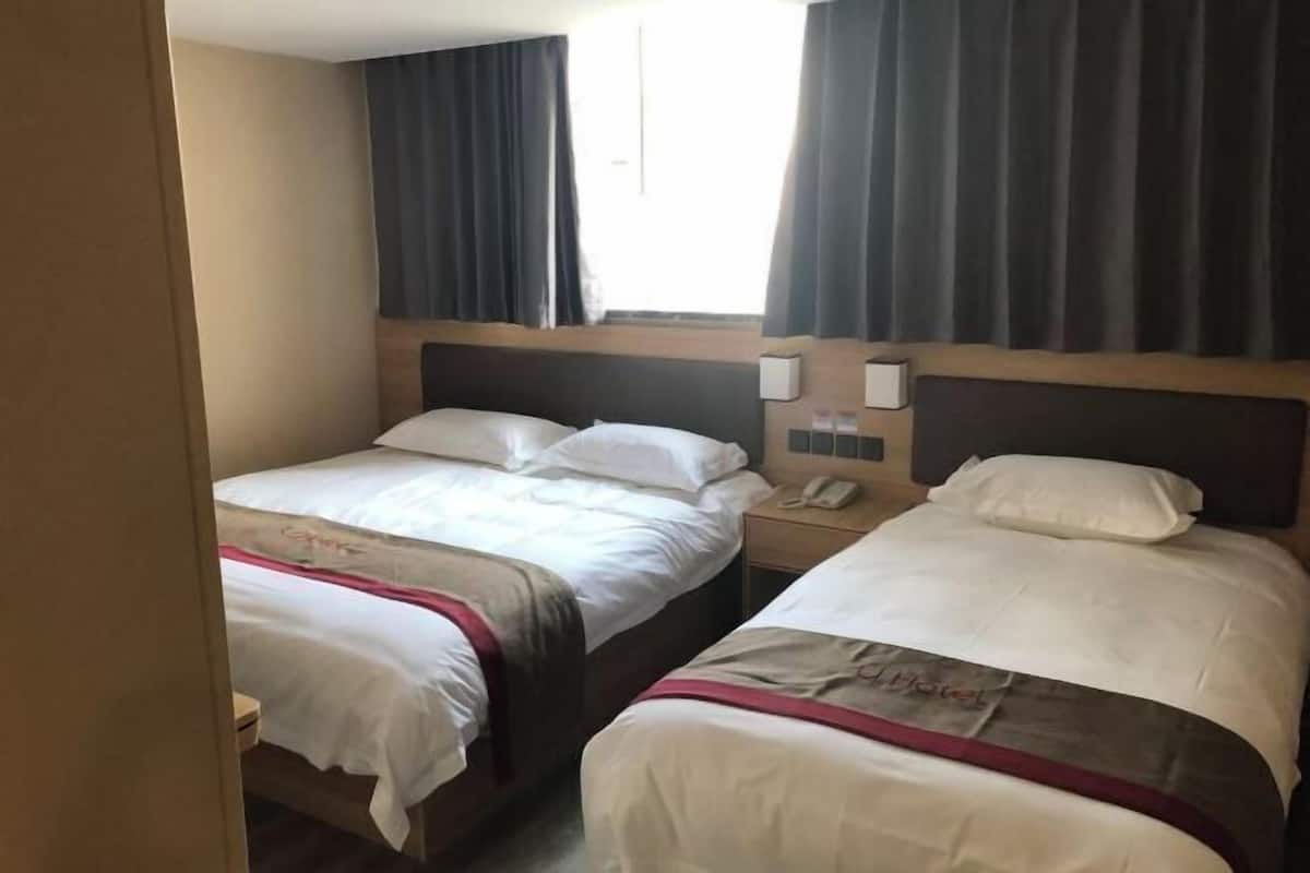 Une chambre d’hôtel avec deux lits, un téléphone sur la table de chevet et une fenêtre avec des rideaux.