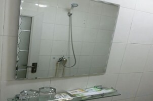 Un baño con cabina de ducha de vidrio, un espejo y un estante de vidrio con artículos de aseo.