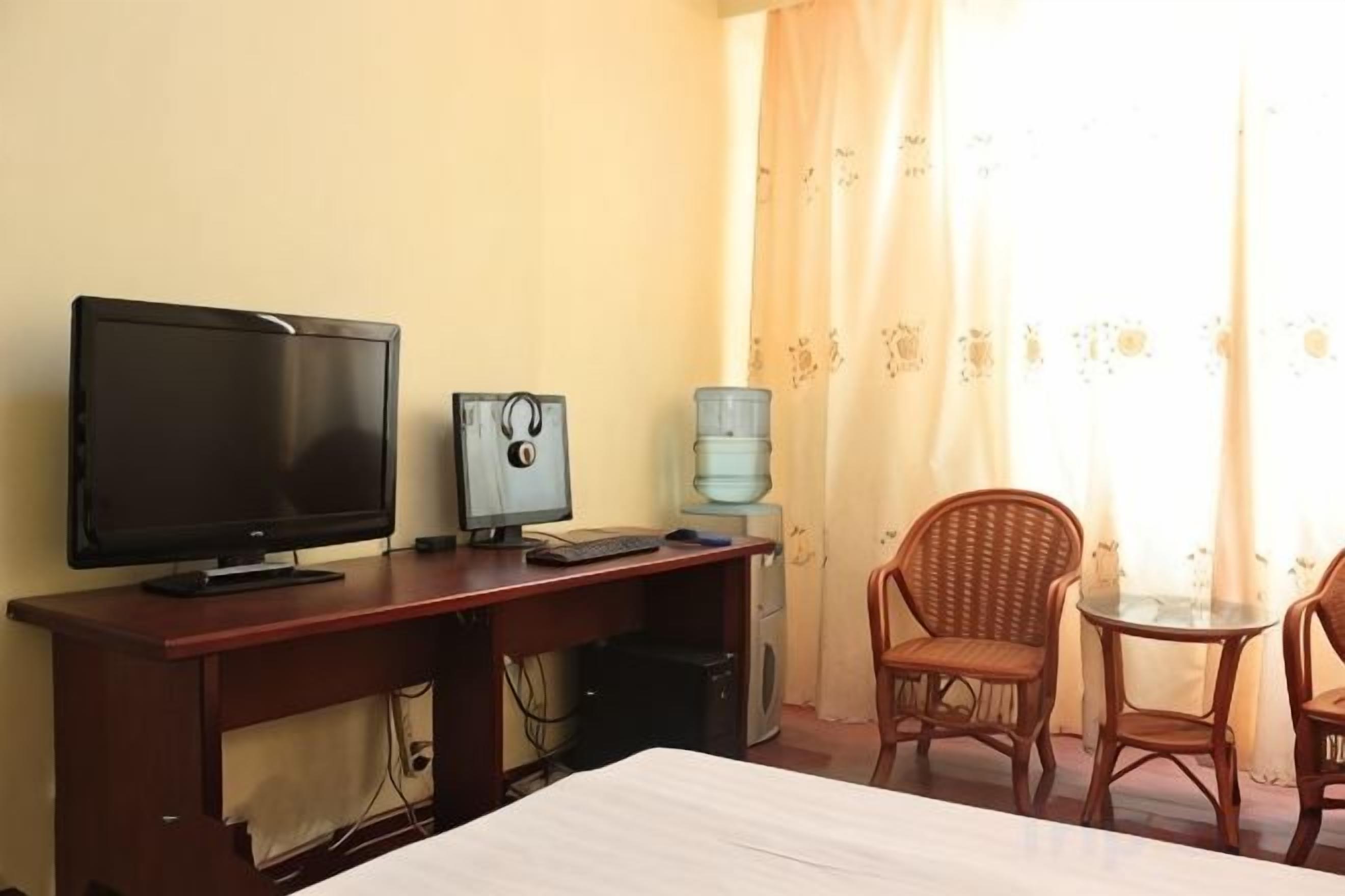 Una habitación de hotel con una cama, un escritorio con una computadora, un televisor y dos sillas de mimbre.