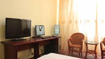 A hotel room with a bed, a desk with a computer, a television, and two wicker chairs.