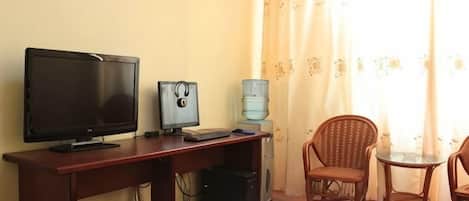 A hotel room with a bed, a desk with a computer, a television, and two wicker chairs.