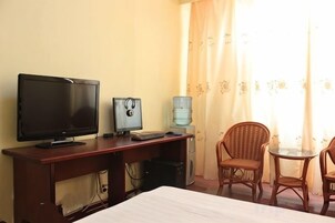 Una habitación de hotel con una cama, un escritorio con una computadora, un televisor y dos sillas de mimbre.
