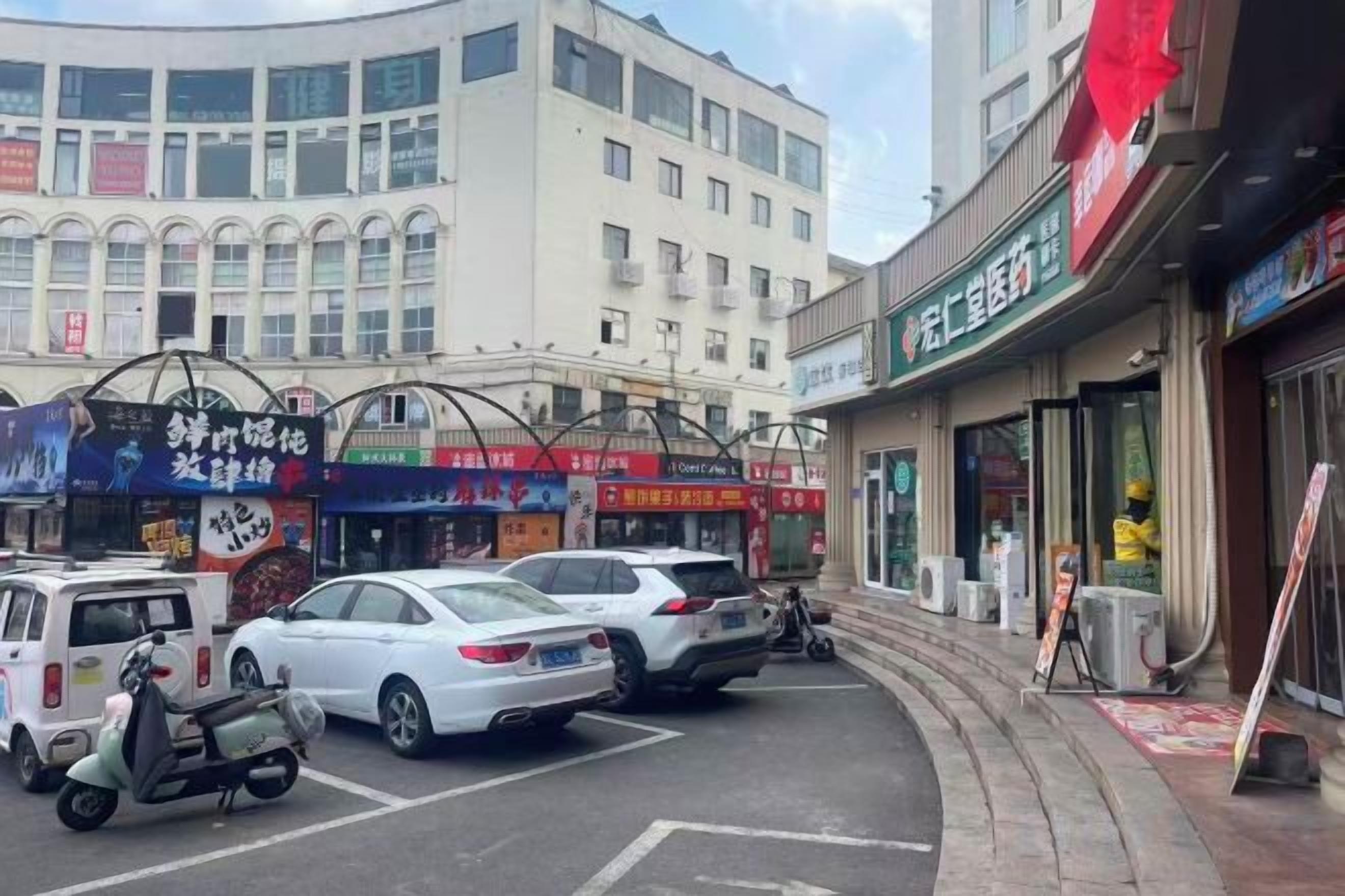 Una calle con coches estacionados y un edificio con varias tiendas.