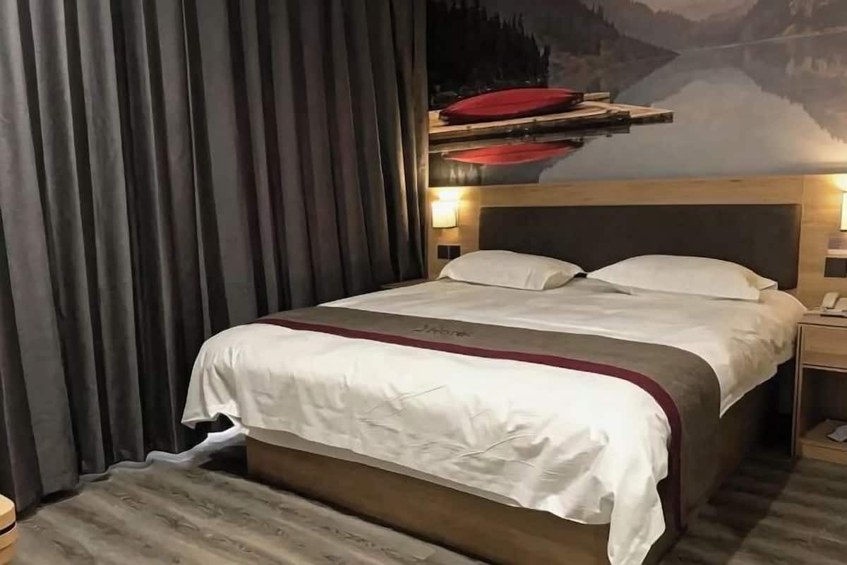 Une chambre d’hôtel avec un lit, des rideaux, une table de chevet et une étagère fixée au mur sur laquelle se trouve un objet rouge.