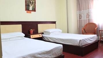 A hotel room with two single beds, a wooden headboard, a small table with a red cup, and a chair.