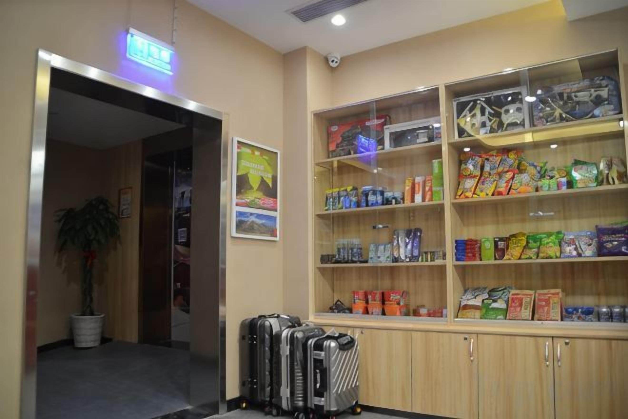 Un vestíbulo de hotel con una recepción, una planta y estantes llenos de aperitivos y artículos de aseo.