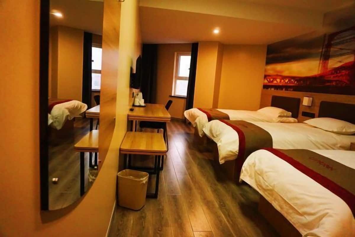 Une chambre d’hôtel avec un plancher en bois, un bureau avec une chaise, deux lits, un miroir et une fenêtre.