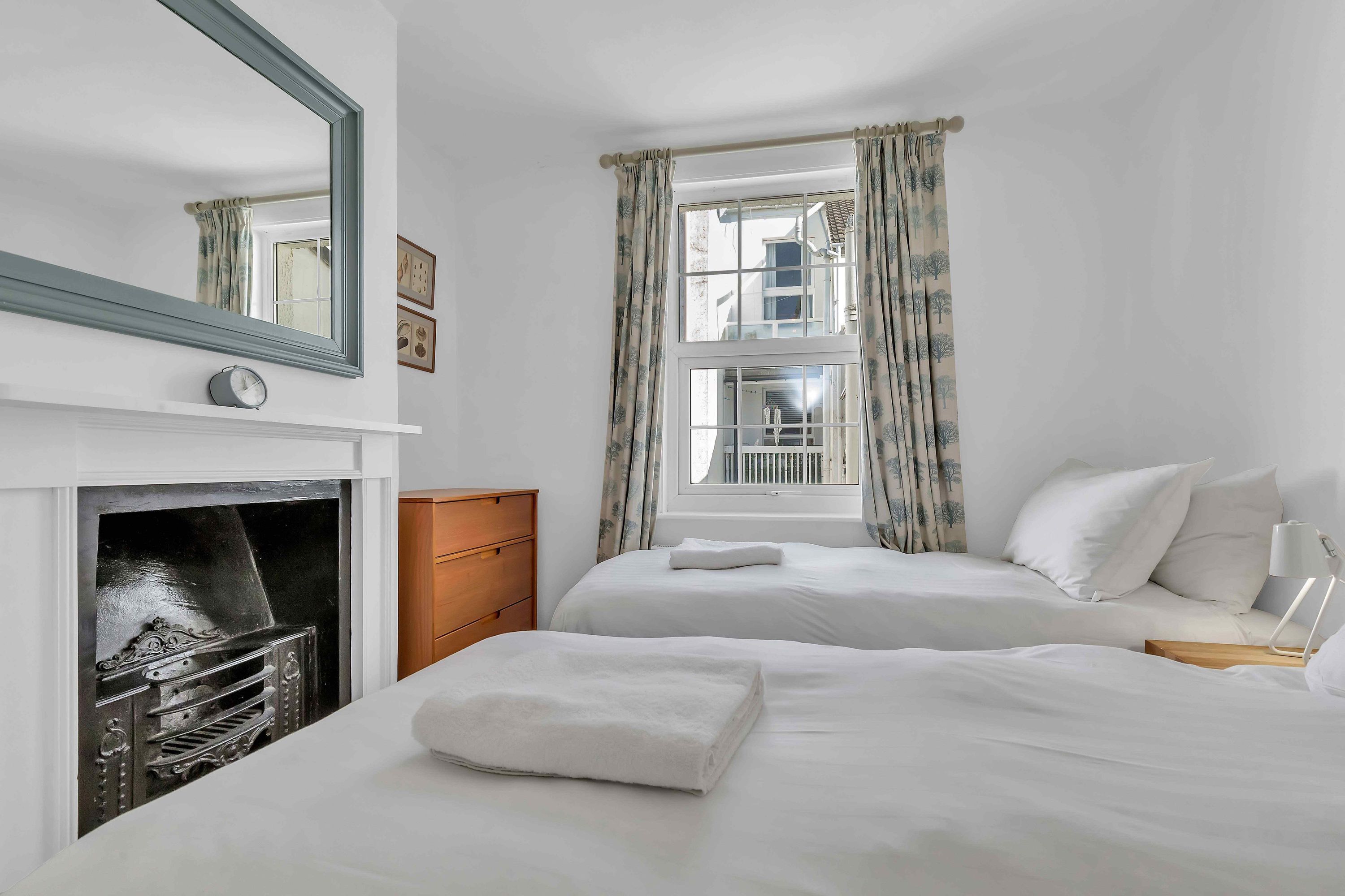 A hotel room with two beds, a fireplace, a large mirror, and a window with curtains.