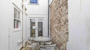 A small outdoor patio with a round metal table and four chairs, a white door, and a brick wall. - Mill Cottage | By My Getaways (Brighton)