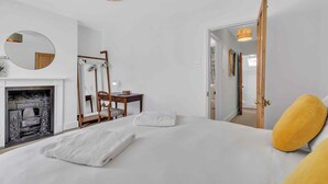 A bedroom with a bed, a mirror, a fireplace, a desk, and a door leading to another room. - Mill Cottage | By My Getaways (Brighton)