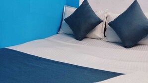 A neatly made bed with a blue and white bedspread, two dark blue pillows, and a folded white towel. - Hotel Sarovar Inn (Ahmedabad)