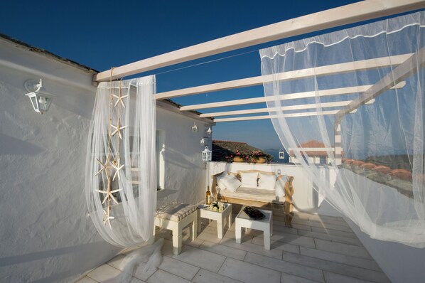 A balcony with a white railing, a white sofa, and a small table with a bottle and flowers. - Althea Boutique Hotel (Alonissos)