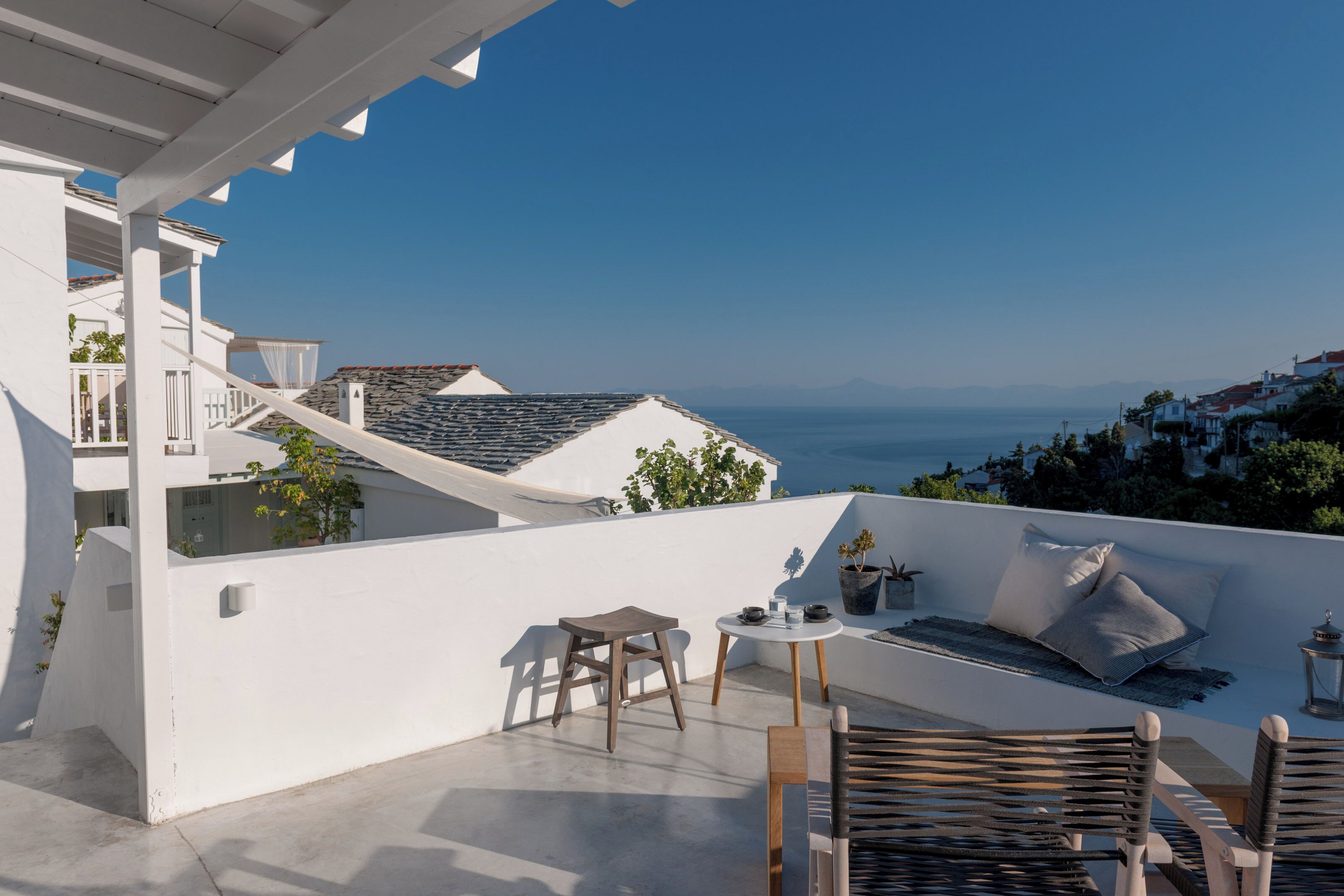 Terraço no telhado com vista para o mar, área de estar com almofadas e uma pequena mesa com uma planta.