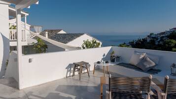 Terraço no telhado com vista para o mar, área de estar com almofadas e uma pequena mesa com uma planta.