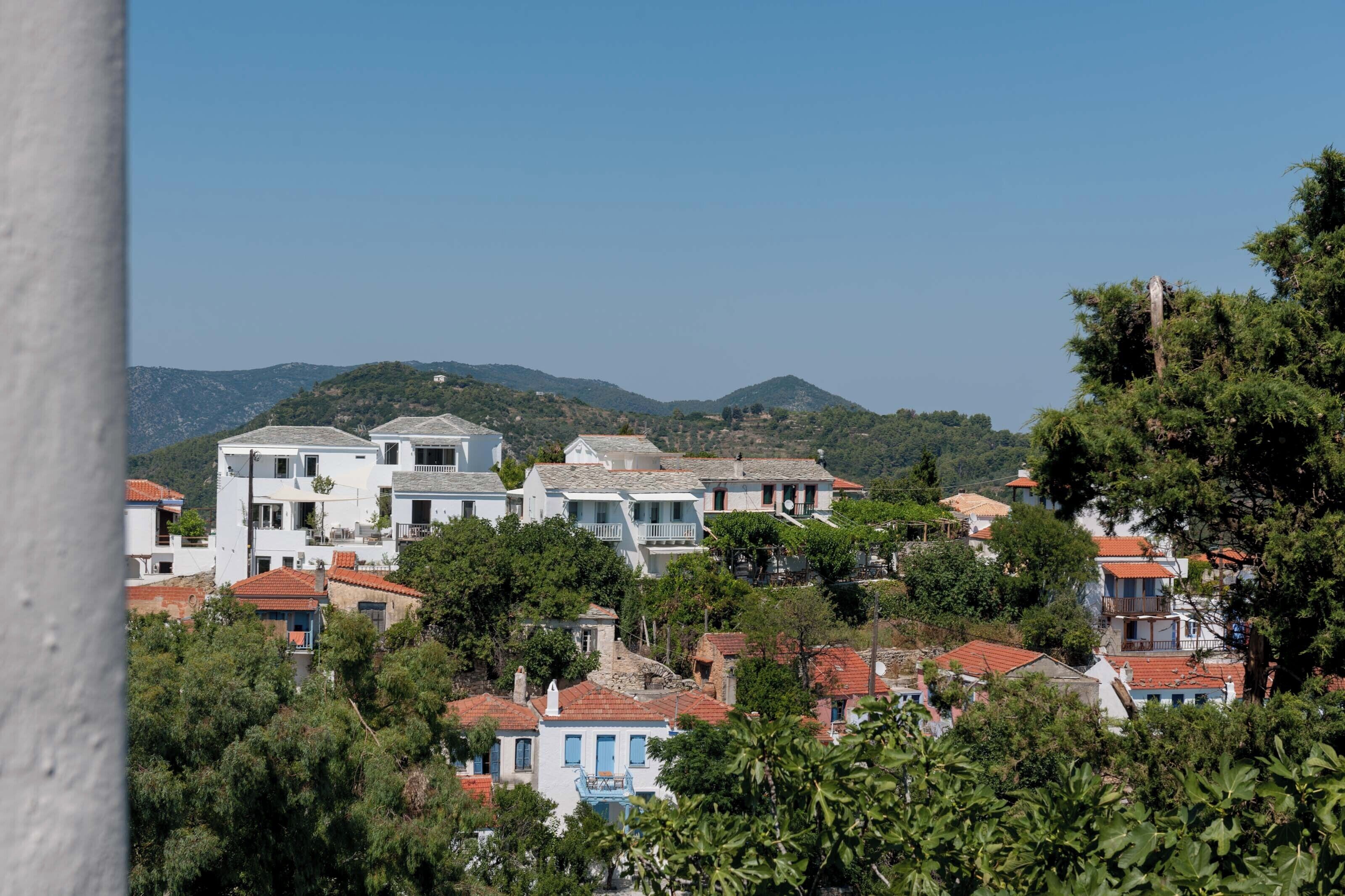 Un pittoresco villaggio costiero con edifici bianchi, tetti in tegole rosse e rigogliosa vegetazione.