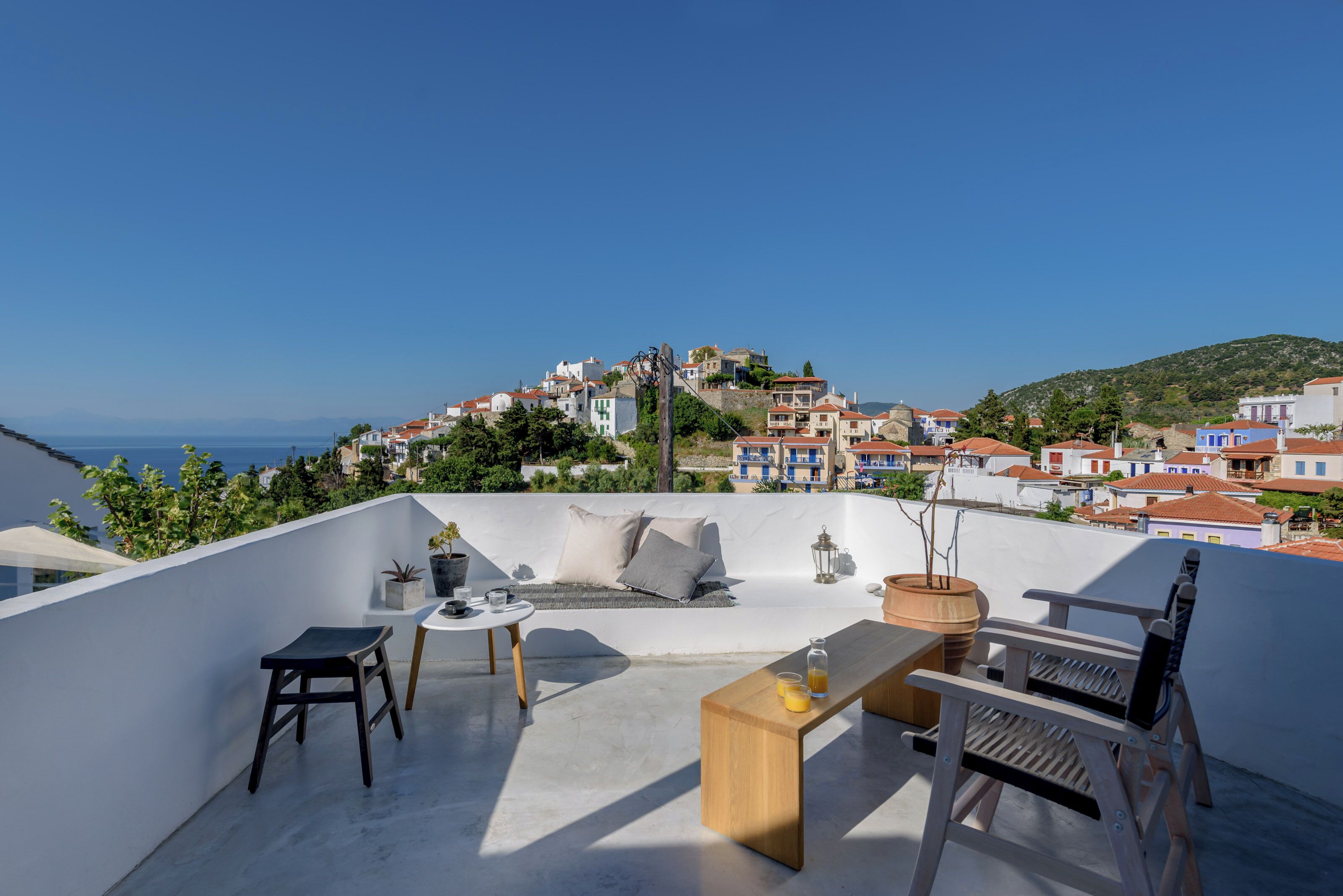 A rooftop terrace with a seating area, a table, and a view of a coastal town.