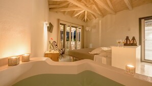 A spa room with a wooden ceiling, a bathtub, a bed, and a small table with candles.