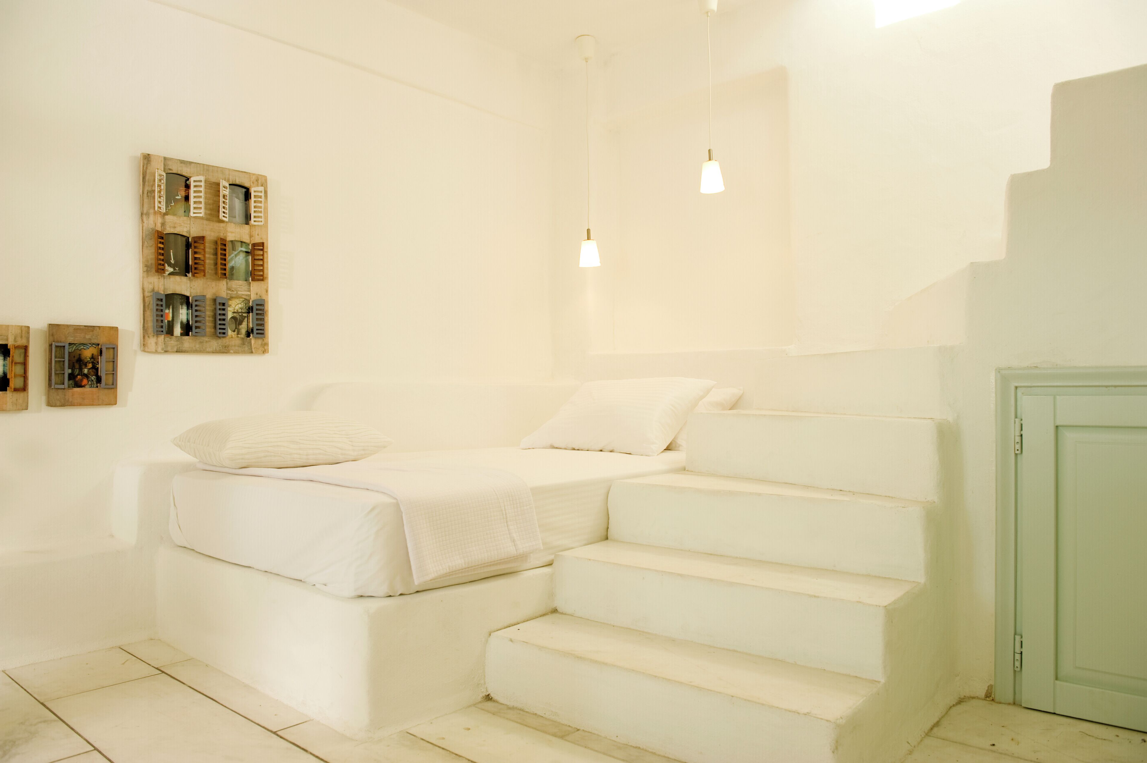 A white room with a bed, a wooden artwork on the wall, and a staircase.