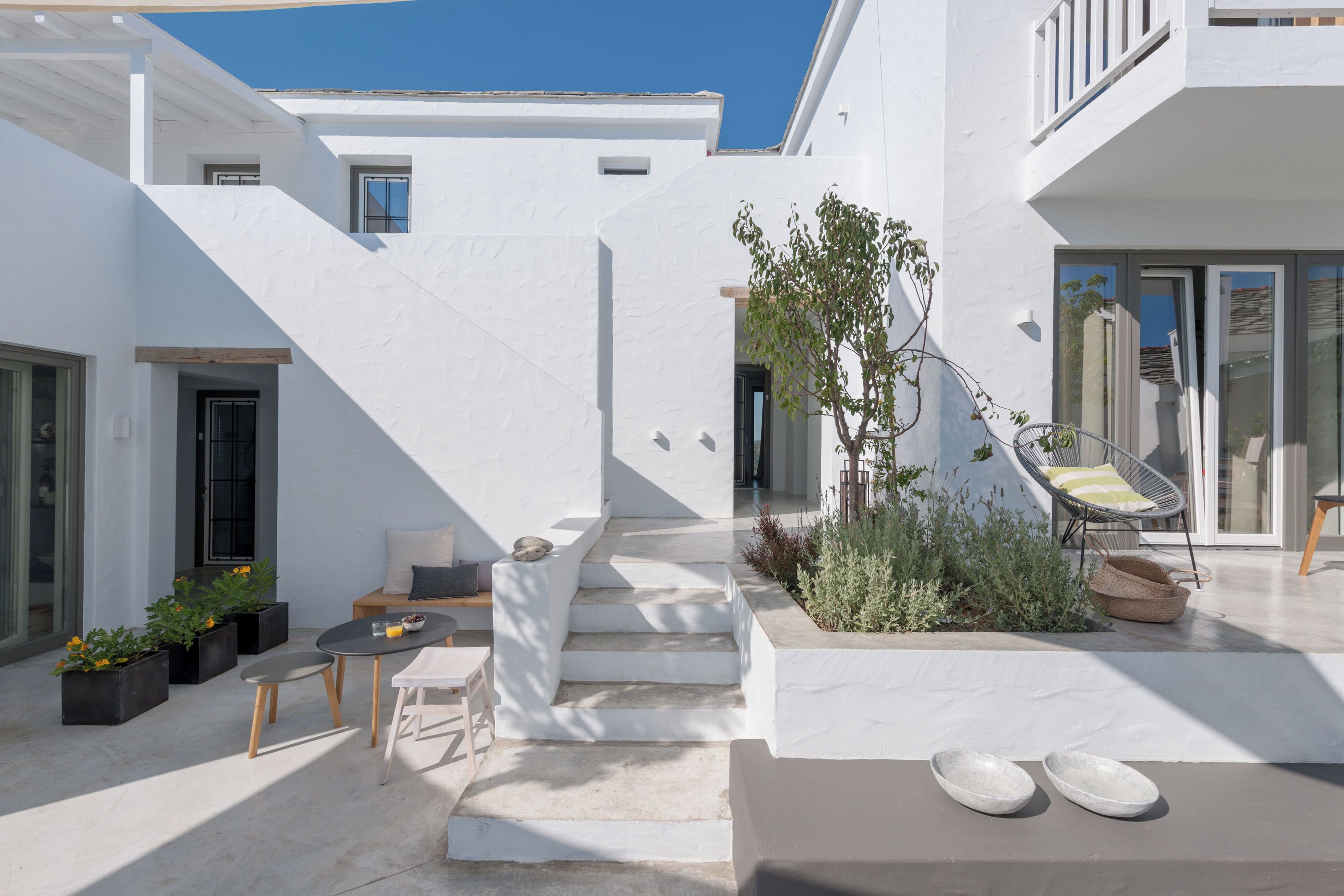 A modern white building with a staircase leading to a balcony, outdoor seating area, and a small garden.